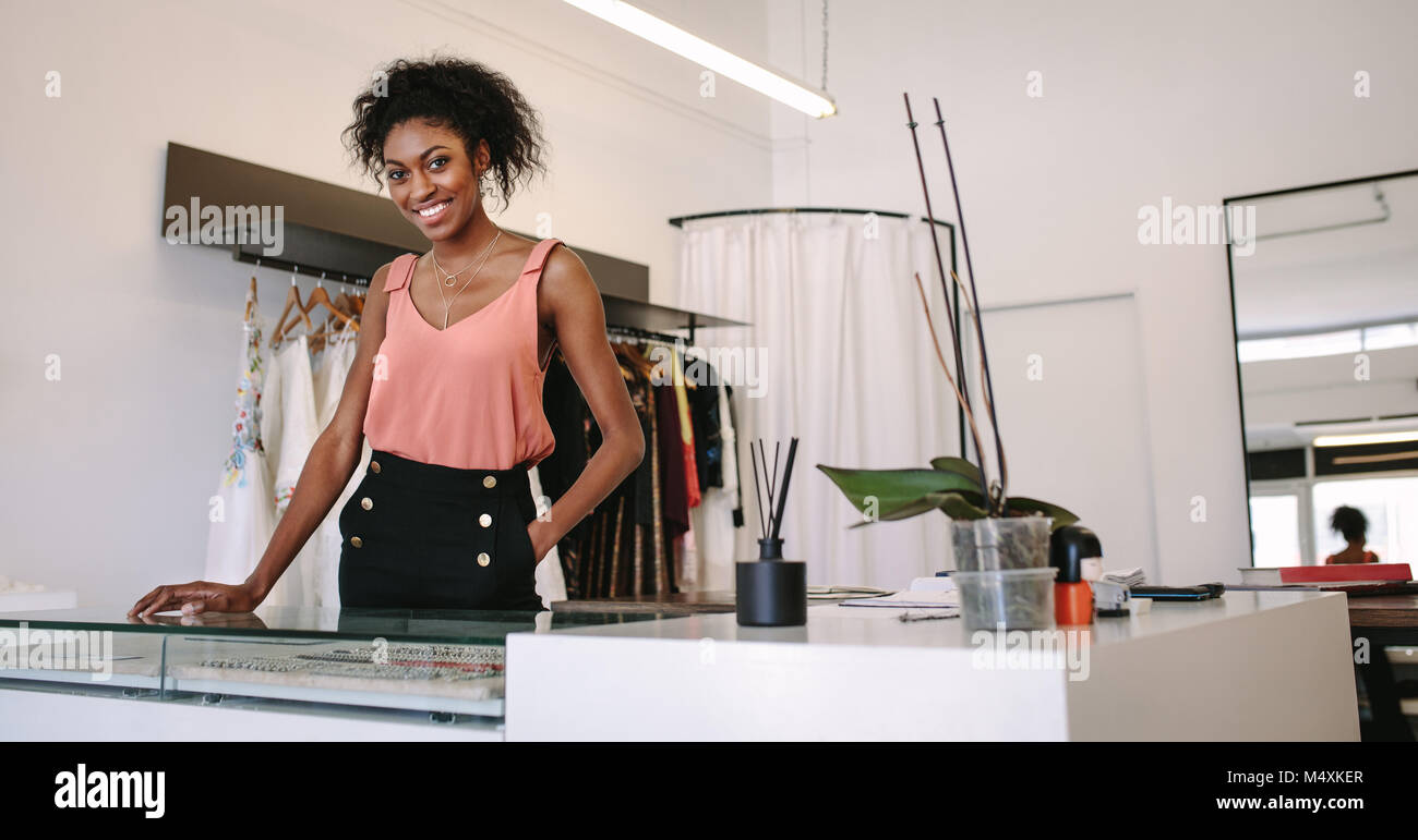 Weibliche Mode Designer stehen an ihrem Schreibtisch in Ihrer Boutique. Weibliche kleid designer in ihr Tuch Shop mit Designer Kleidung auf dem Display. Stockfoto