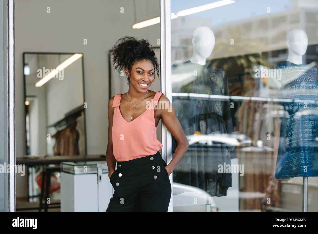 Lächelnd kleid designer in ihr Tuch Shop mit Designer Kleidung auf dem Display. Frau Unternehmer am Eingang ihre Mode Studio. Stockfoto