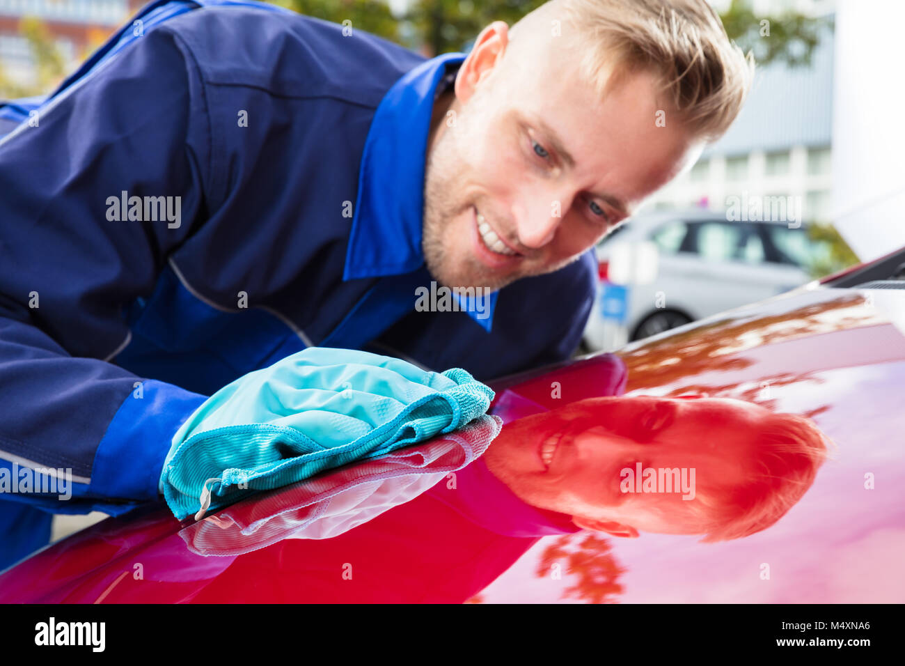 Junge Glücklich männlichen Arbeitnehmers rotes Auto mit Lappen reinigen Stockfoto