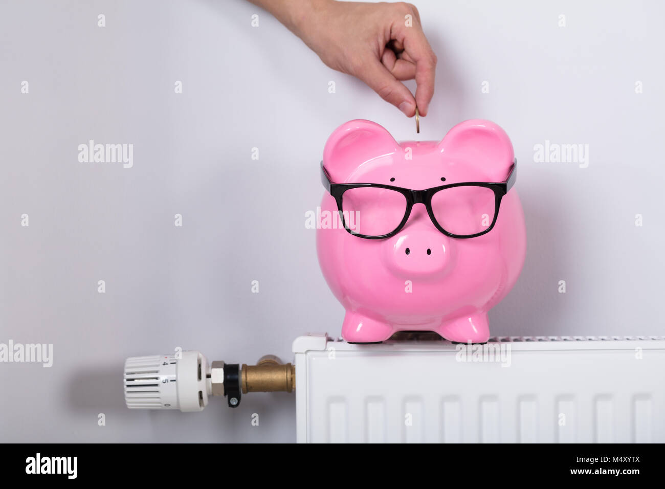 Hand einfügen Münze in Sparschwein am Kühler zu sparen Energiekosten Stockfoto