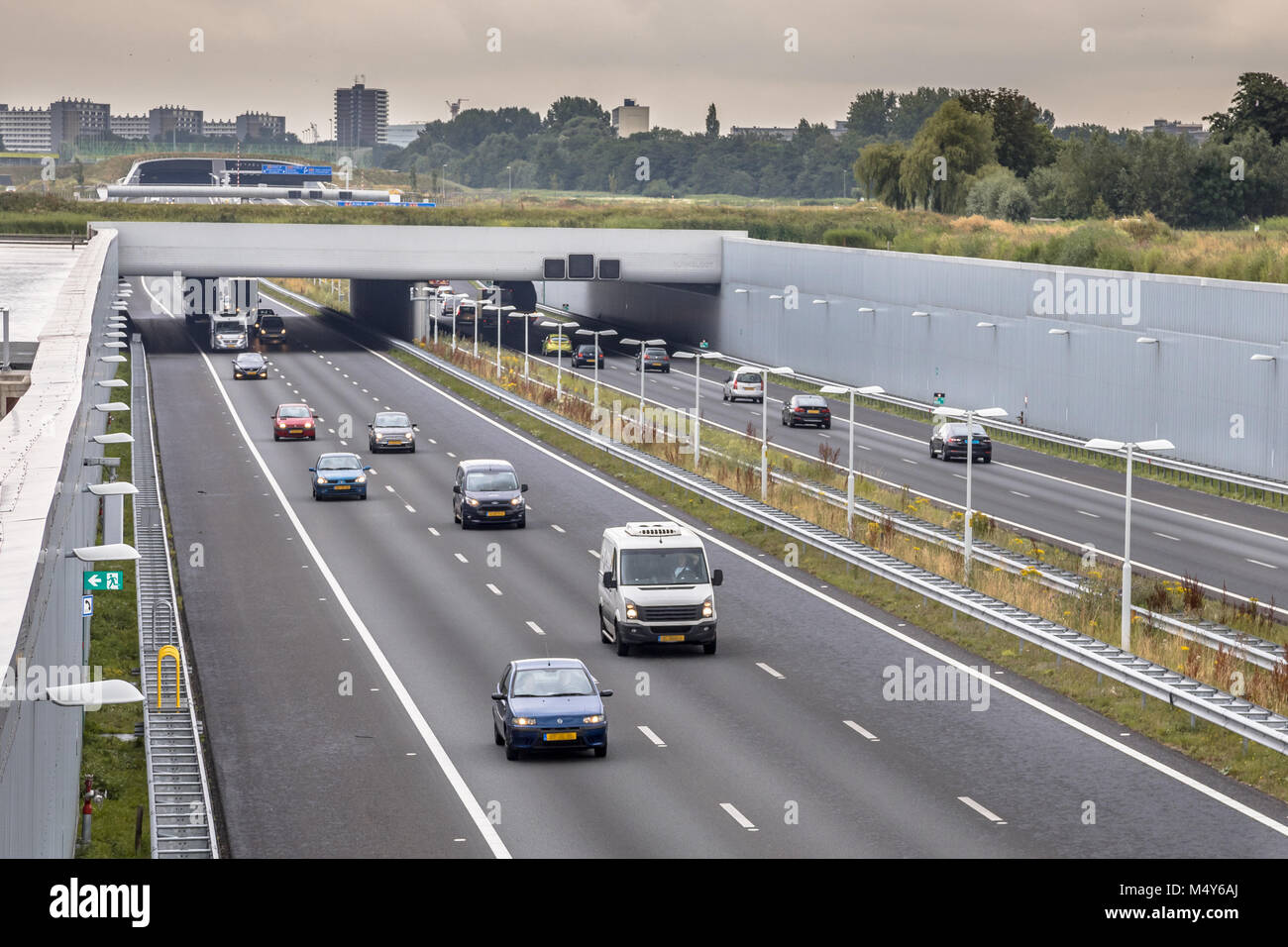 Nachmittag der Verkehr auf der Autobahn A4 in der Nähe von Den Haag Gegend Randstad. Autobahn Kreuzung aquaduct Tunnel mit städtischen Gebiet von Rotterdam im Hintergrund, Niederlande. Stockfoto