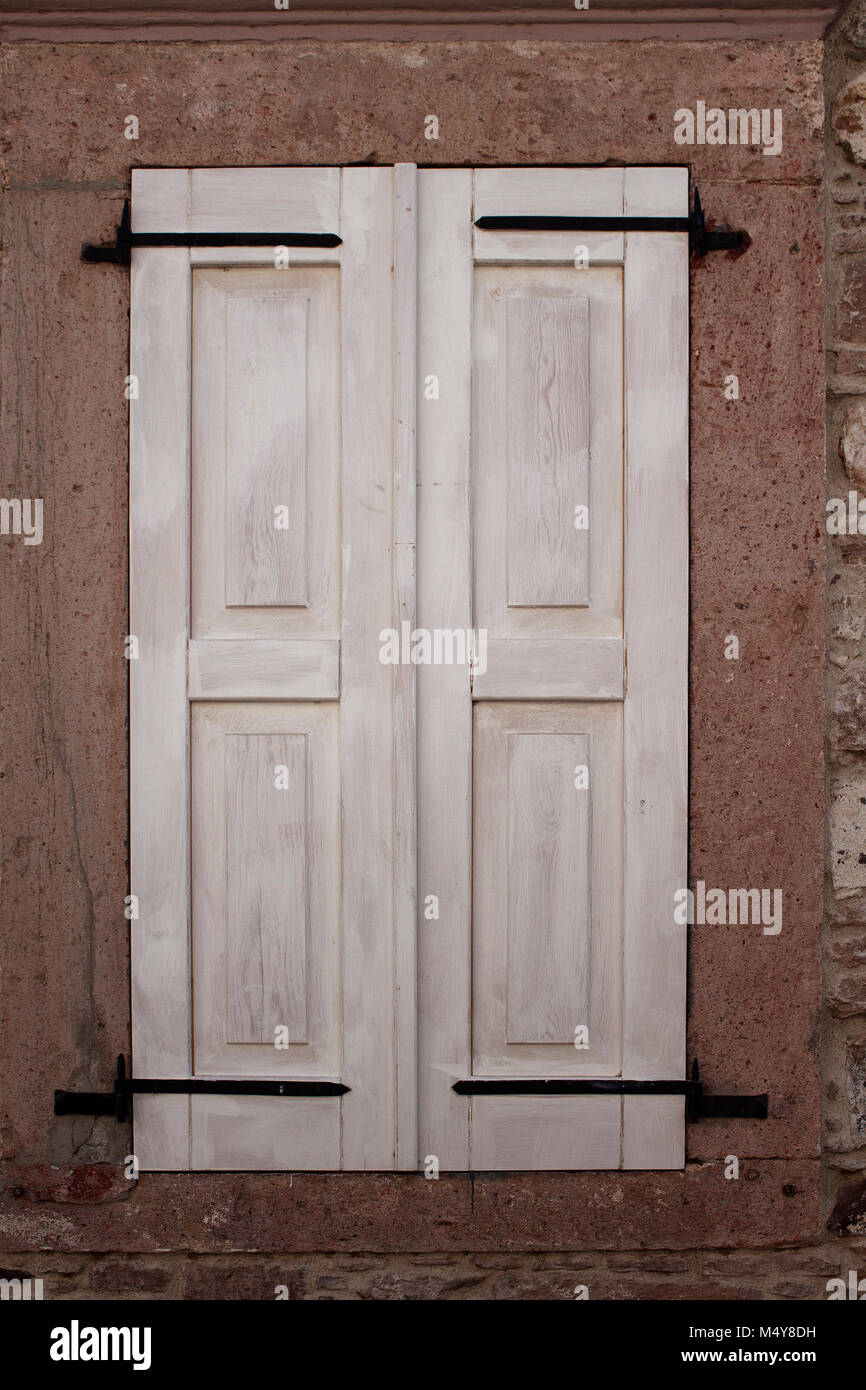Nahaufnahme der geschlossenen Fenster mit weißen Fensterläden aus Holz und alten Steinmauer. Stockfoto