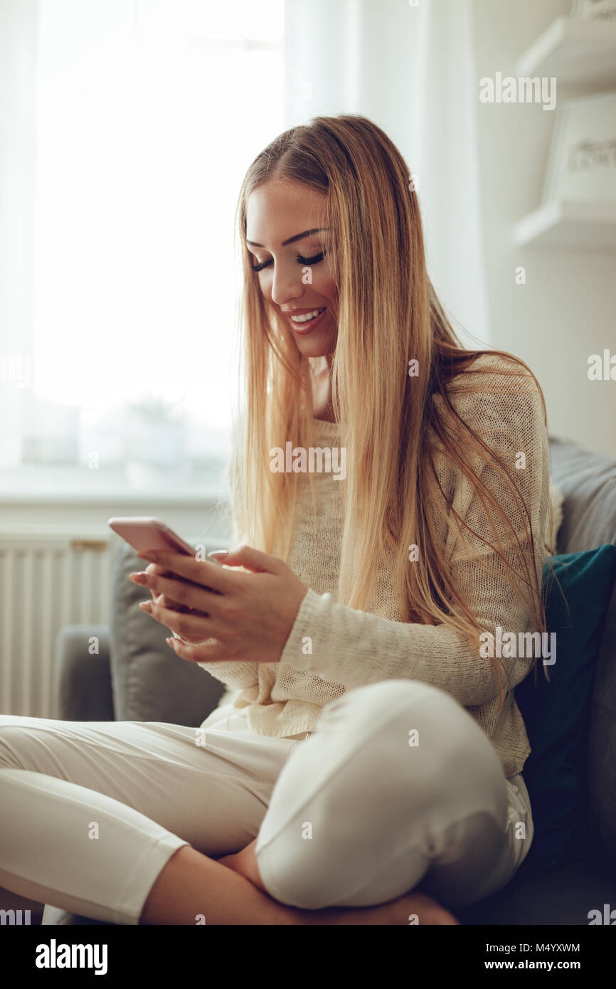Schöne junge lächelnde Frau am Haus entspannen und Surfen im Netz auf einem Smartphone. Stockfoto