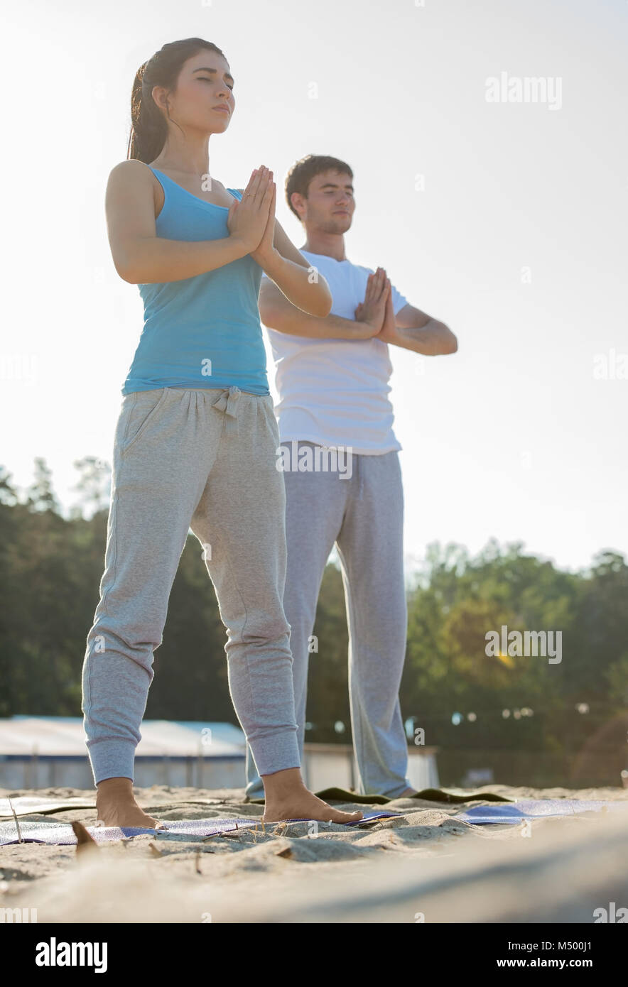 Fitness, Sport, Freundschaft und Lifestyle-Konzept - lächelnde paar machen Meditation Yoga-Übungen am Strand am Morgen Stockfoto