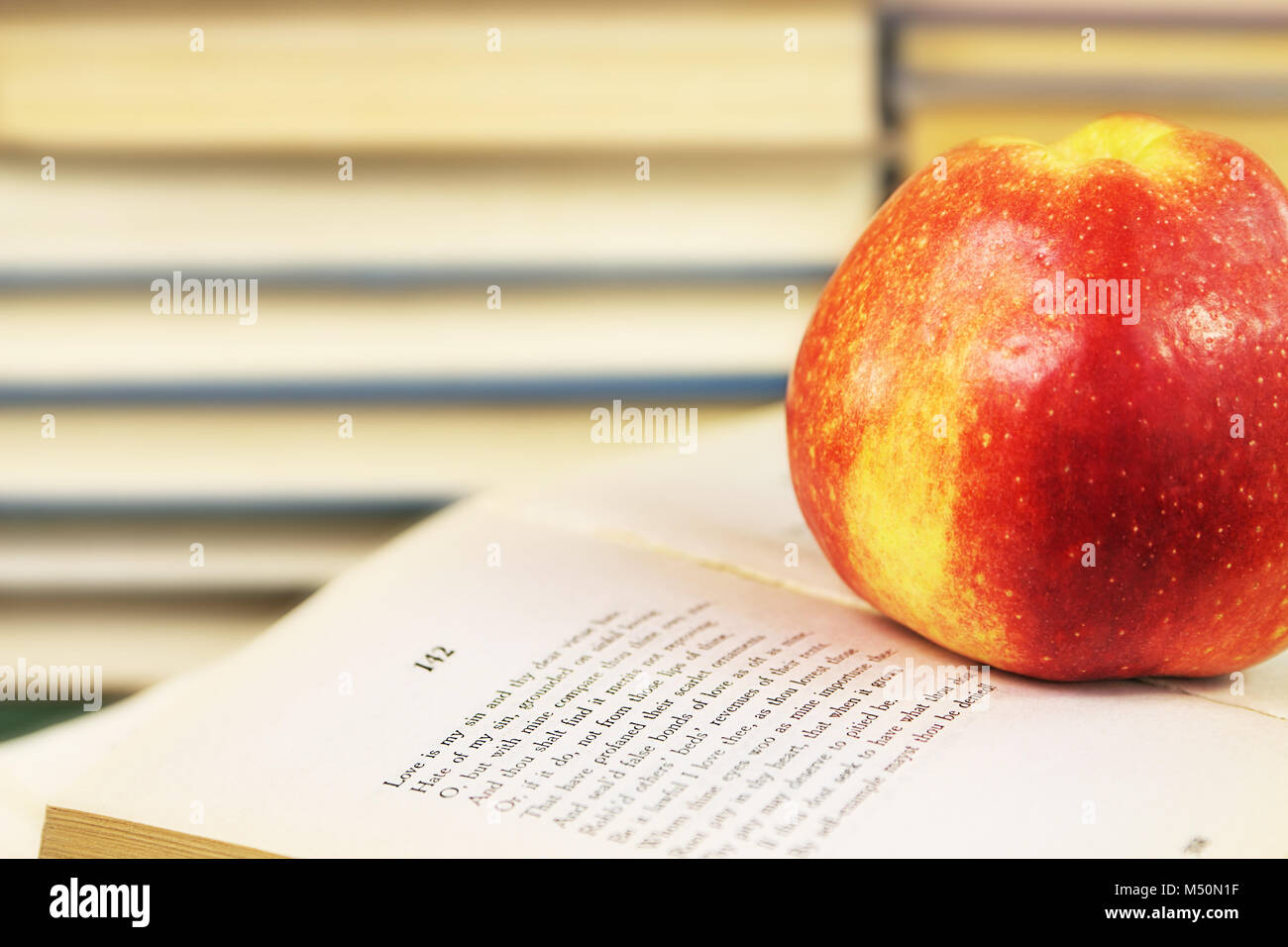 Ein großer roter Apfel auf ein offenes Buch mit Shakespeares Sonette auf dem Hintergrund einer Regal mit Büchern Stockfoto