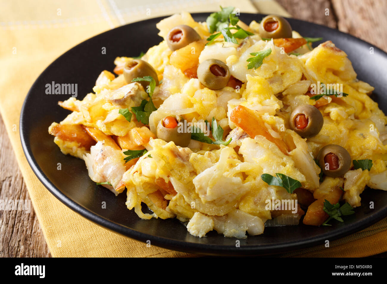 Gebratene Stockfisch mit Kartoffeln, Zwiebeln und ein Omelett auf einer Platte close-up auf einem Tisch. Horizontale Stockfoto