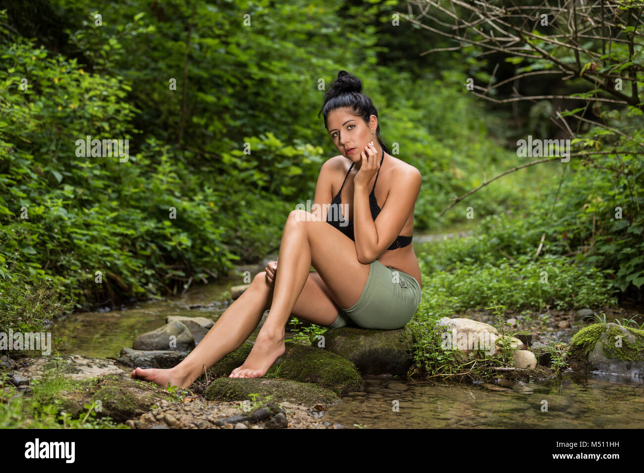 Junge Frau sitzt auf einem Stein im Stream Stockfoto