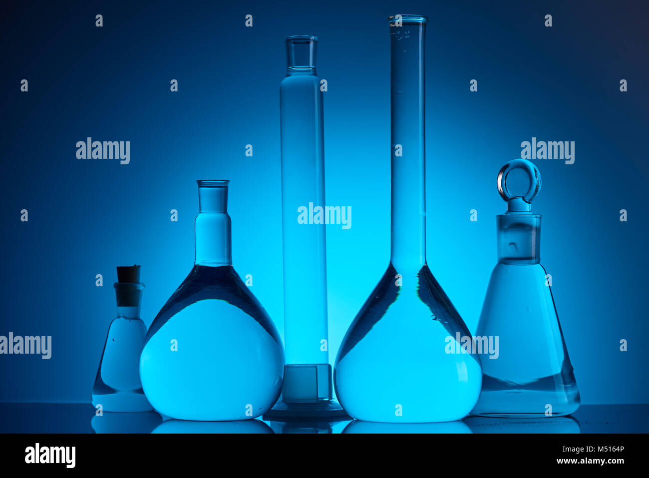 Verschiedene Glaskolben mit Flüssigkeit im chemischen Labor auf Blau Stockfoto