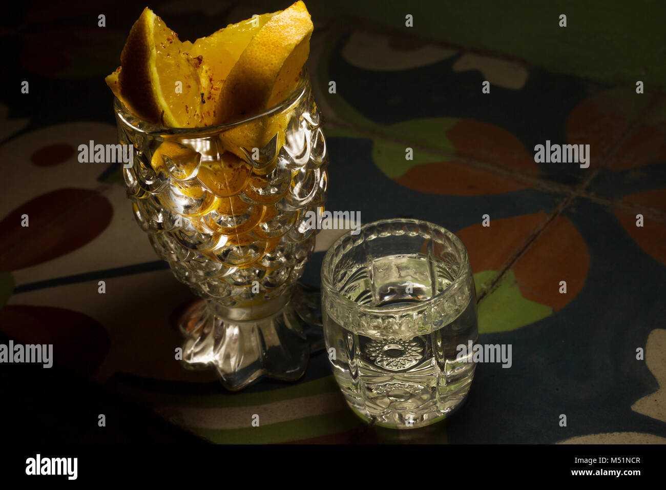 Mexikanische Mezcal in einem Glas neben Crystal Becher mit Scheiben von Orangen auf eine mexikanische Fliesen Stockfoto