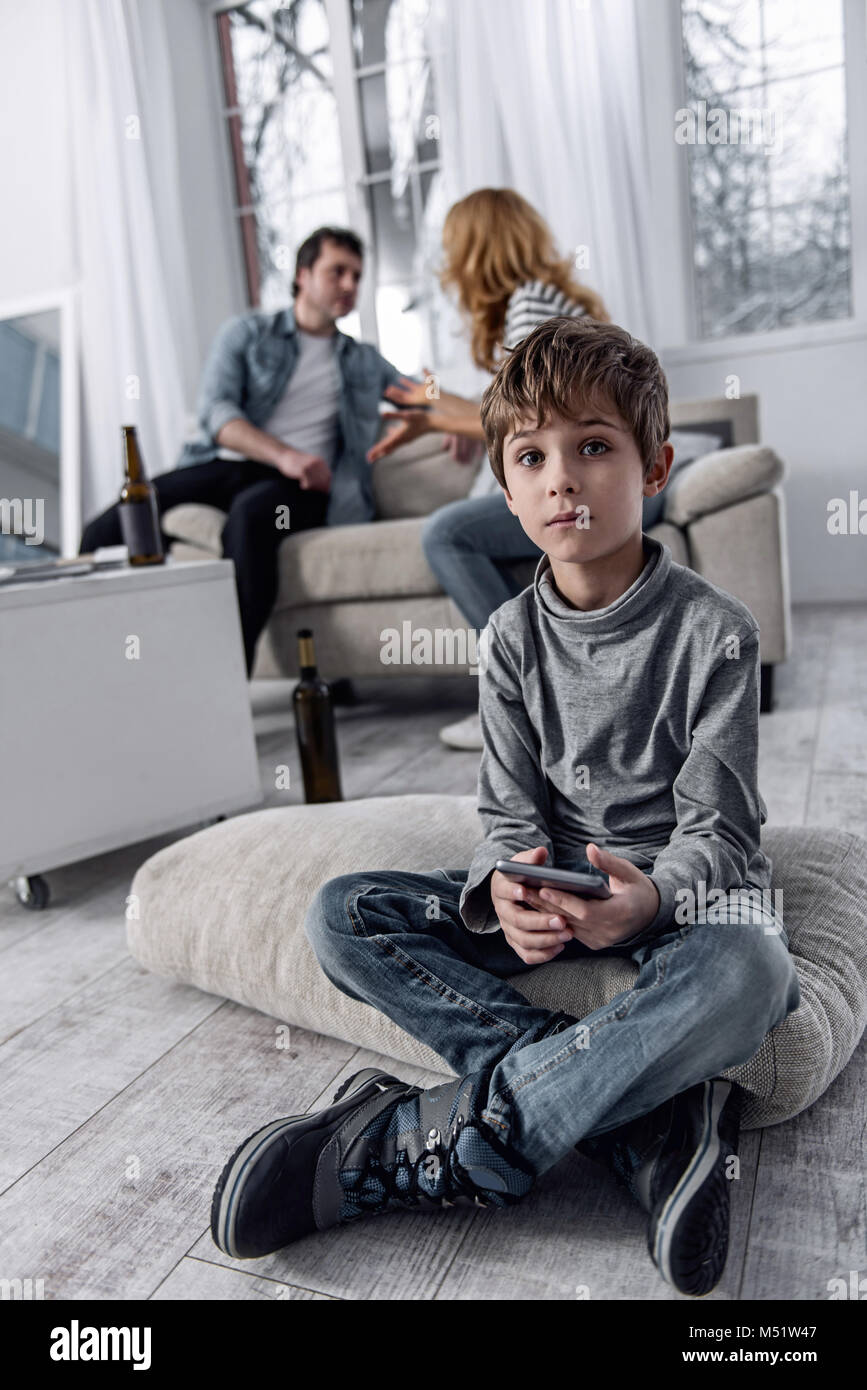 Kleiner Junge sitzt mit einem Smartphone, während seine Eltern erhalten geschieden Stockfoto