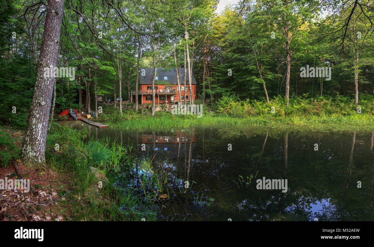 Morgen Sonnenschein badet ein modernes anmelden Urlaub zu Hause mit einem Teich, Dock und Kanus in idyllischer Lage umgeben von Wäldern, Frieden und Ruhe umgeben. Stockfoto