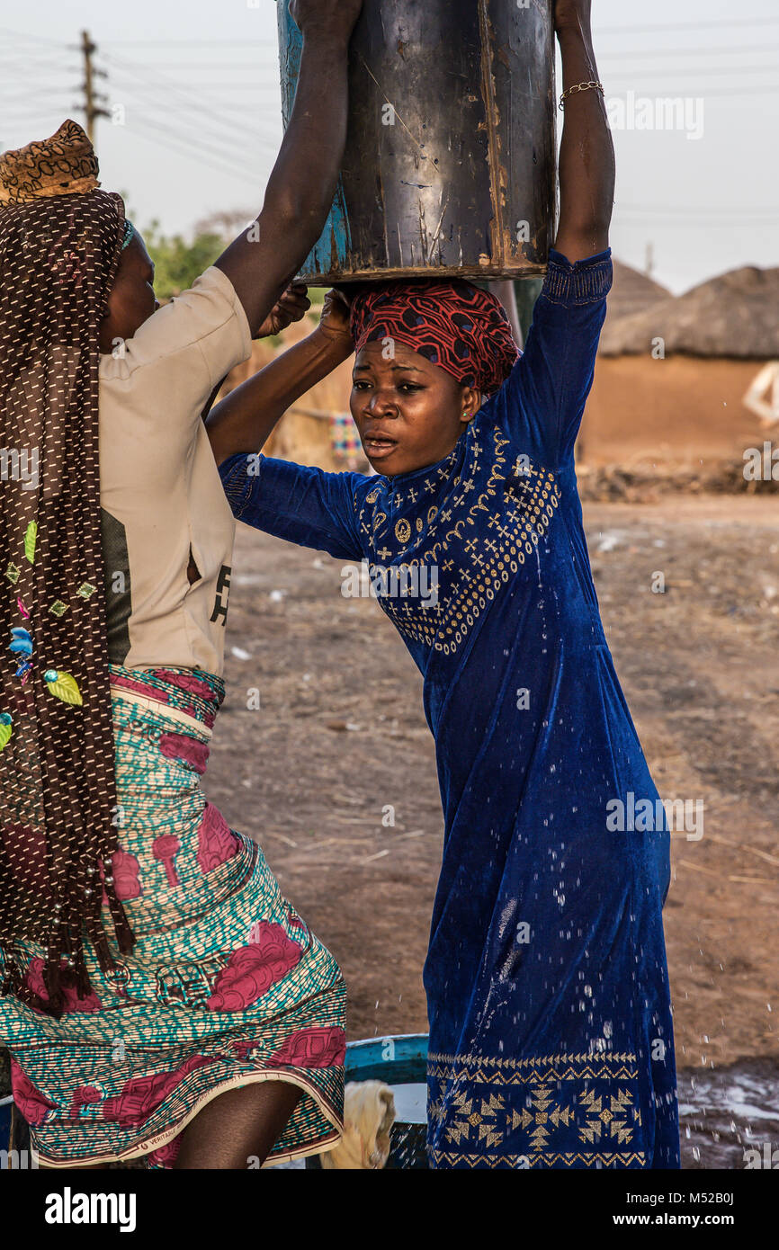 Eine Frau kämpft mit der Schwere des Wasserbehälters in dem abgelegenen Dorf Nepilsi, 30 km außerhalb von Tamale im Norden Ghanas. Frauen in Ghana alle ihre Habseligkeiten auf dem Kopf tragen. Es ist unglaublich, die gewichten sie in der Lage sind, zu tragen. Die menschliche Befreiung Stiftung begann die Arbeit an einem Gut mit frischem Wasser für das Dorf vor zwei Jahren, besuchten wir die positiven Auswirkungen auf die Gemeinschaft hat. Diese Bereiche des Ghana sind so abgelegen und der Armut sind einige der niedrigsten der Welt. Stockfoto