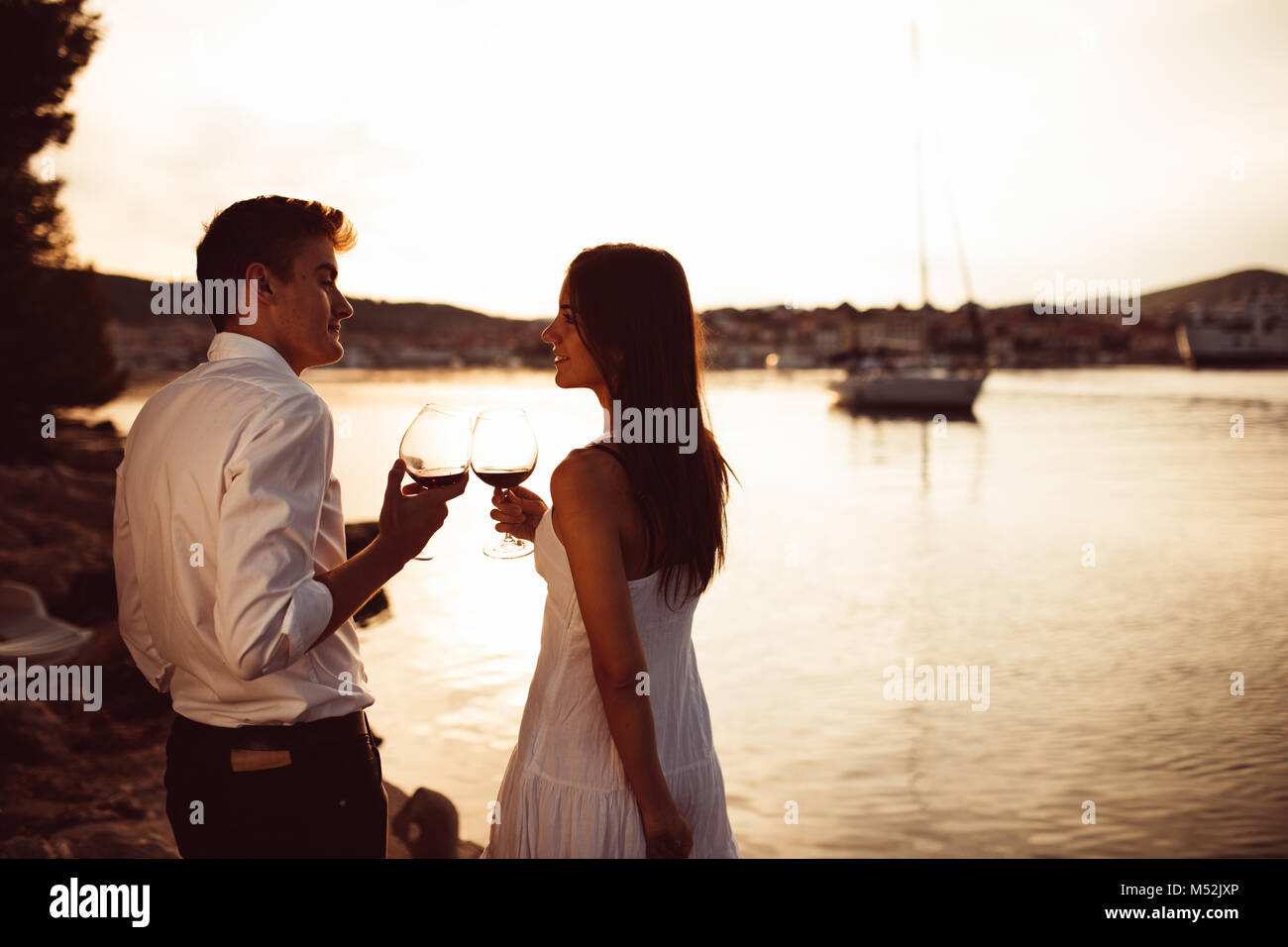 Romantisches Paar trinken Wein bei Sonnenuntergang an einer Pier auf einem Meer. Romanze. Zwei Menschen, die sich einen romantischen Abend bei einem Glas Wein in der Nähe des Meeres. Stockfoto