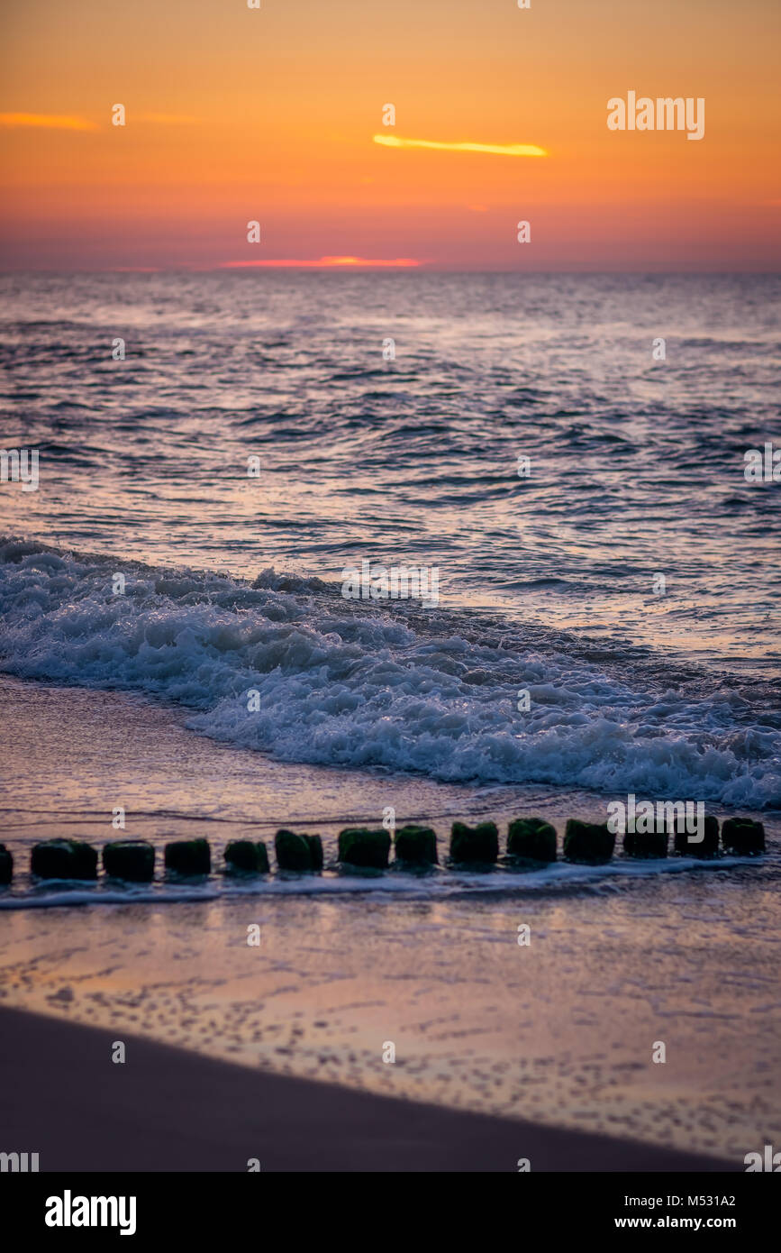 Alte hölzerne Wellenbrecher am Strand bei Sonnenuntergang Stockfoto