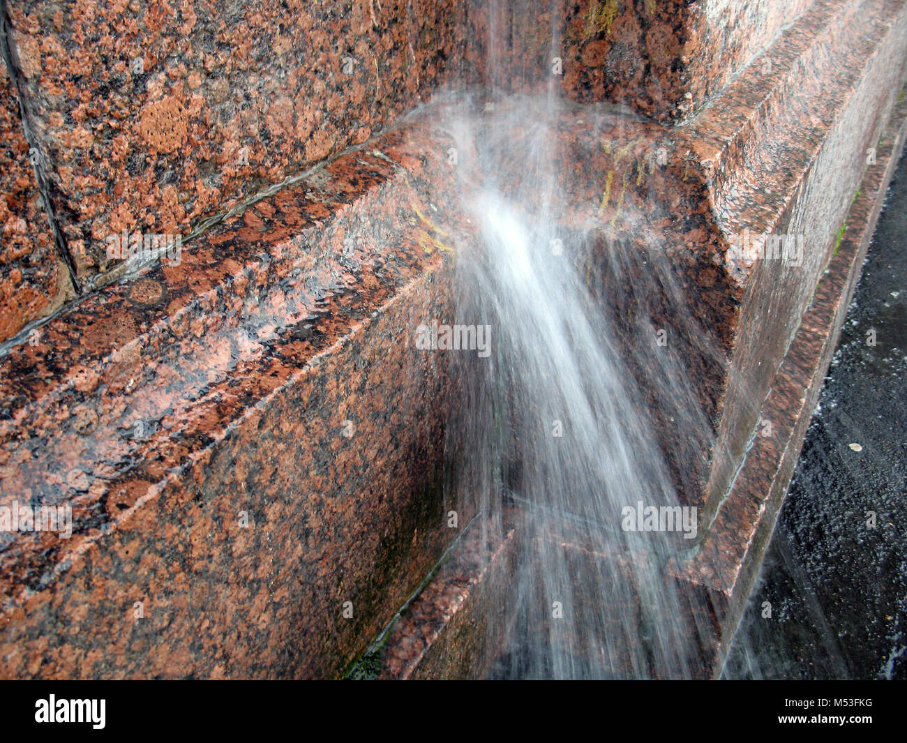 Ein starker Strahl Wasser aus dem abflußrohr auf der granitmauer während der regensturm Stockfoto