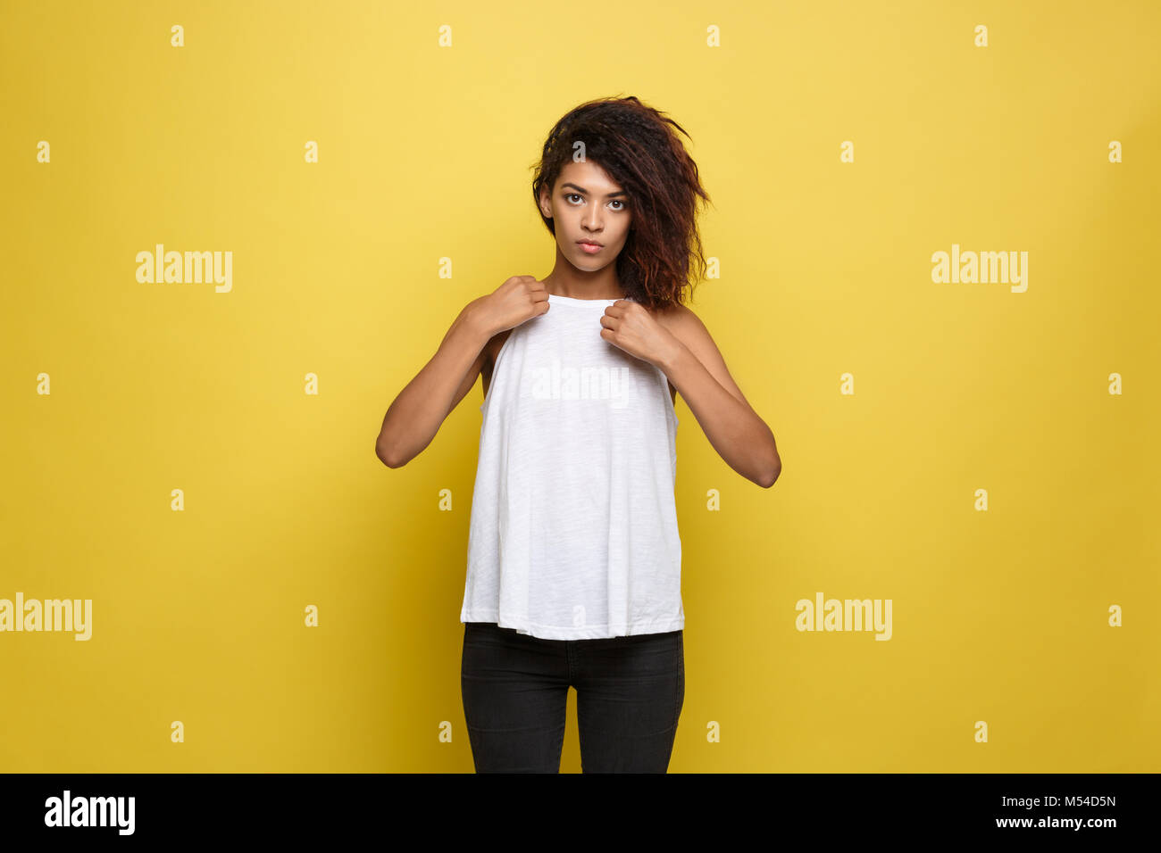 Schöne attraktive Afrikanische amerikanische Frau und kleidete sich ihr weisses T-Shirt. Gelbe studio Hintergrund. Platz kopieren Stockfoto