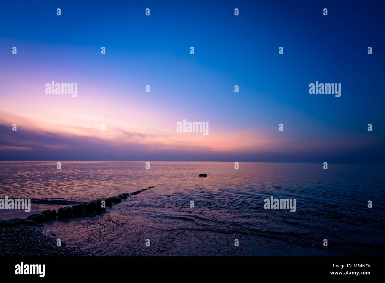 Alte hölzerne wellenbrecher an der Küste bei Sonnenuntergang Stockfoto