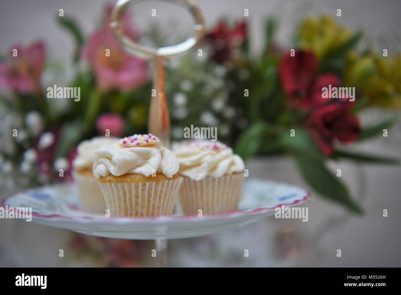 Essen von Cupcakes auf einem vintage Kuchen stand mit frischen Blumen Stockfoto