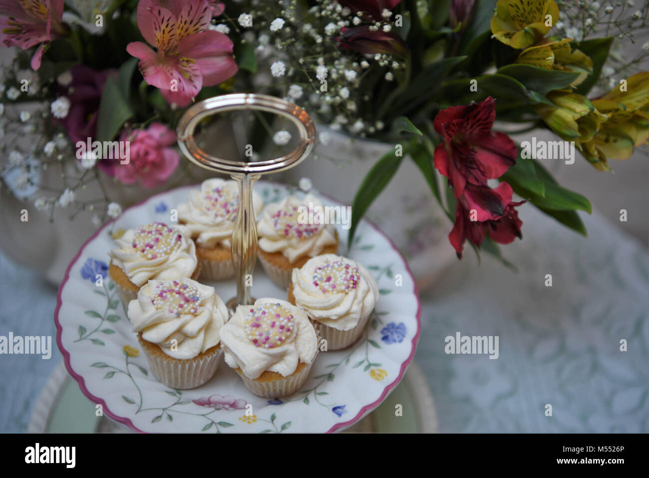 Essen von Cupcakes auf einem vintage Kuchen stand mit frischen Blumen Stockfoto