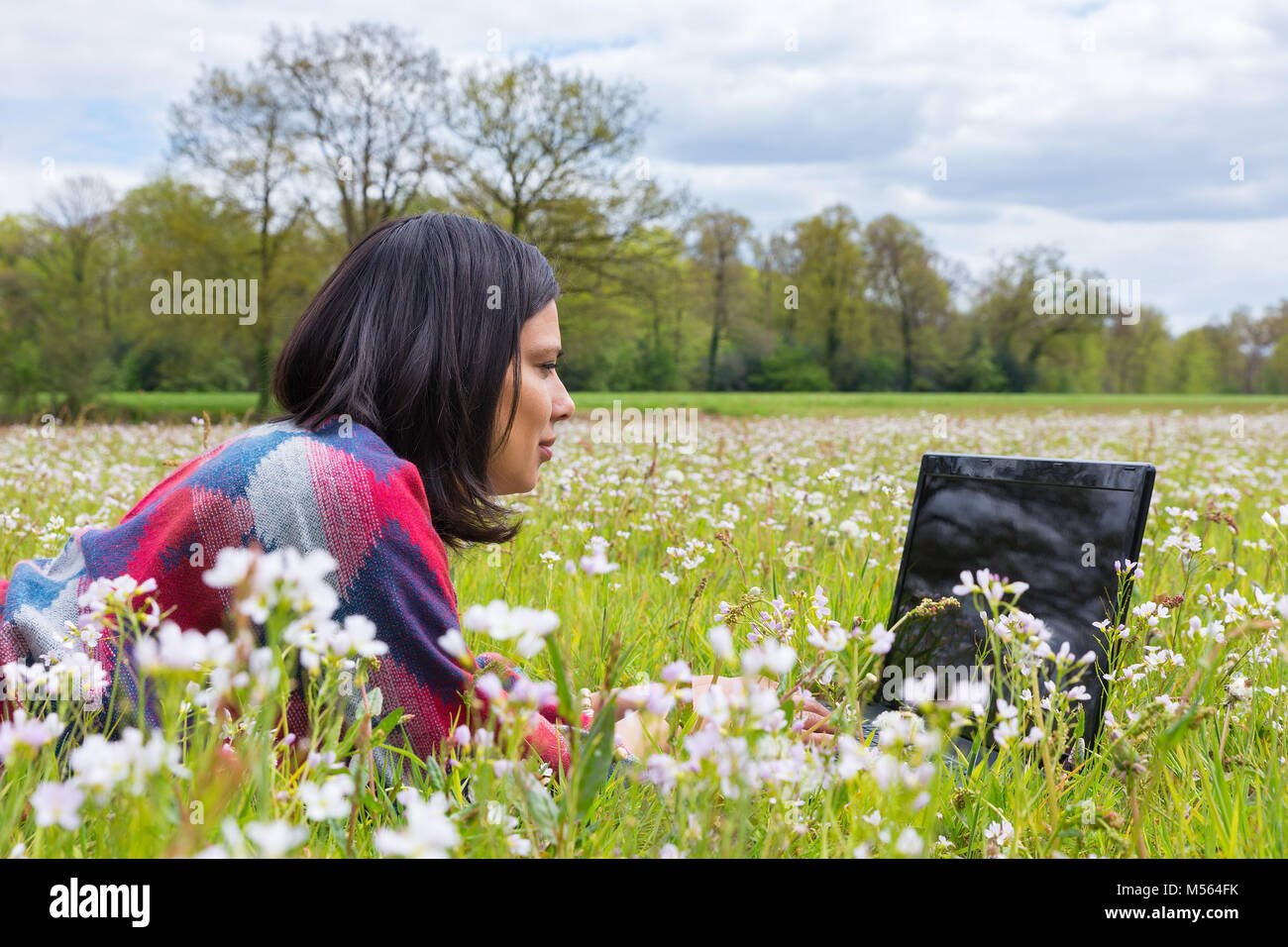 Frau mit Laptop im Gras liegend mit Blumen Stockfoto