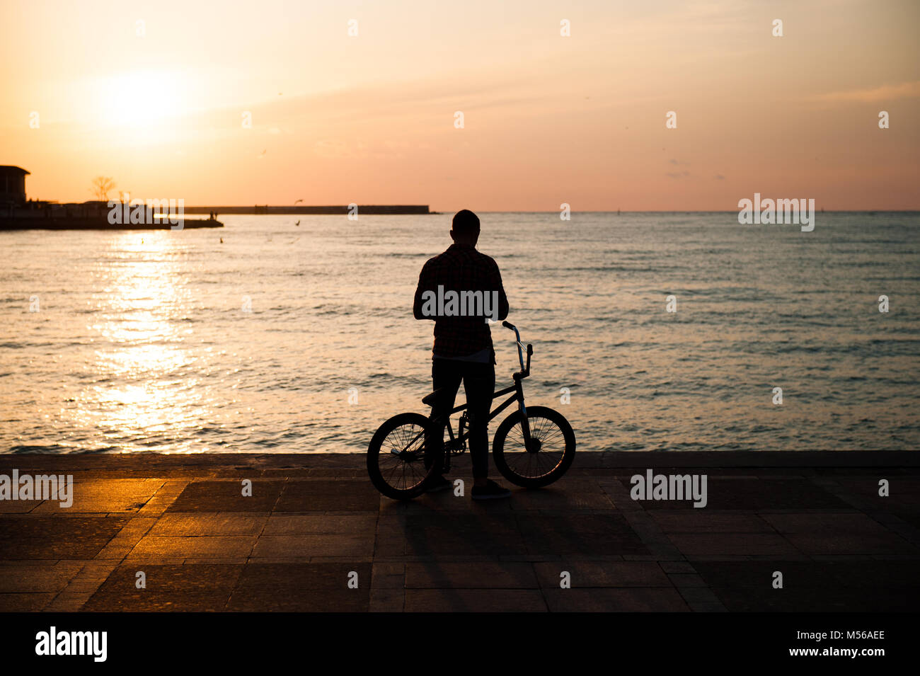 Die Silhouette eines jungen Mannes mit dem Fahrrad gegen das Meer, in der Stadt Stockfoto