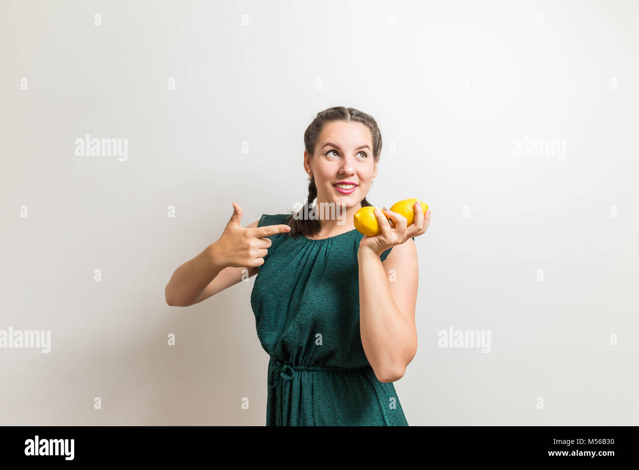 Schöne Mädchen Punkte um Früchte und Zitronen und sieht auf weißem Hintergrund zu Seite Stockfoto