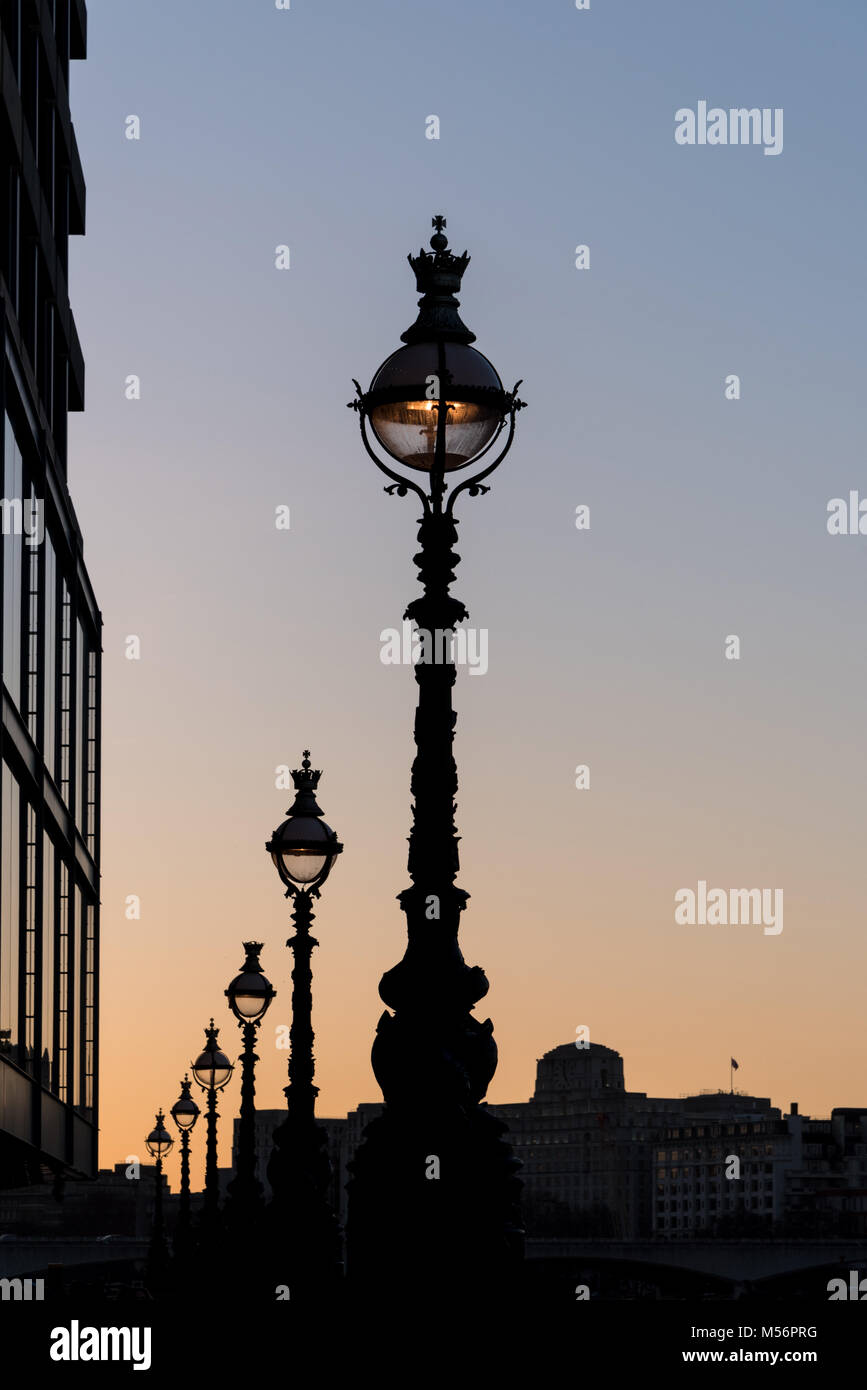 Atmosphärische Linie der eleganten Straße Lampe leuchtet Silhouette gegen einen klaren Himmel bei Sonnenuntergang mit Gebäuden Stockfoto