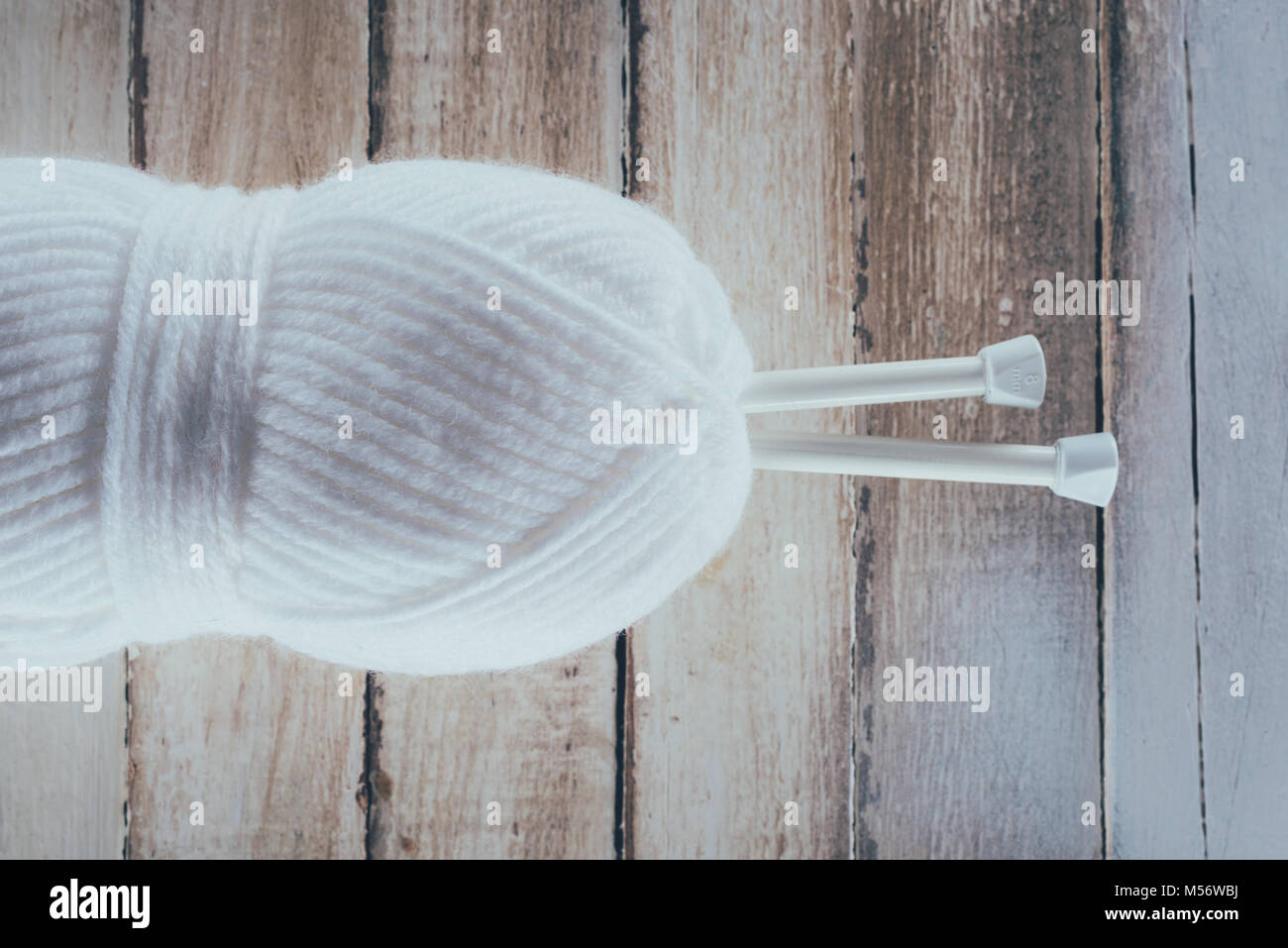 Blick von oben auf die weisse Garn und Stricknadeln auf hölzernen Hintergrund Stockfoto
