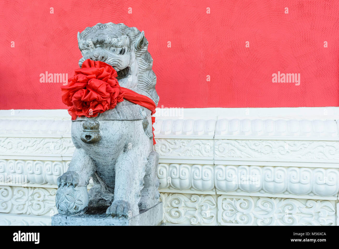 Traditionelle steinerne Statue eines chinesischen Guardian lion (männlich), tragen eine große rote Schleife um den Hals Das chinesische Neujahr zu feiern, vor o veröffentlicht Stockfoto