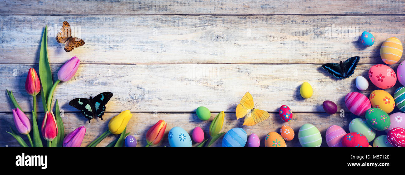 Ostern - Tulpen mit Schmetterlingen und bemalte Eier auf Vintage Plank Stockfoto