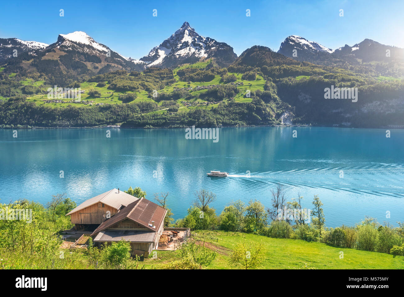 Erstaunlich Frühling Landschaft mit den Alpen Berge, den Walensee mit einem Boot schwimmend auf, und eine alte Scheune auf einer grünen Wiese, an einem sonnigen Tag. Stockfoto