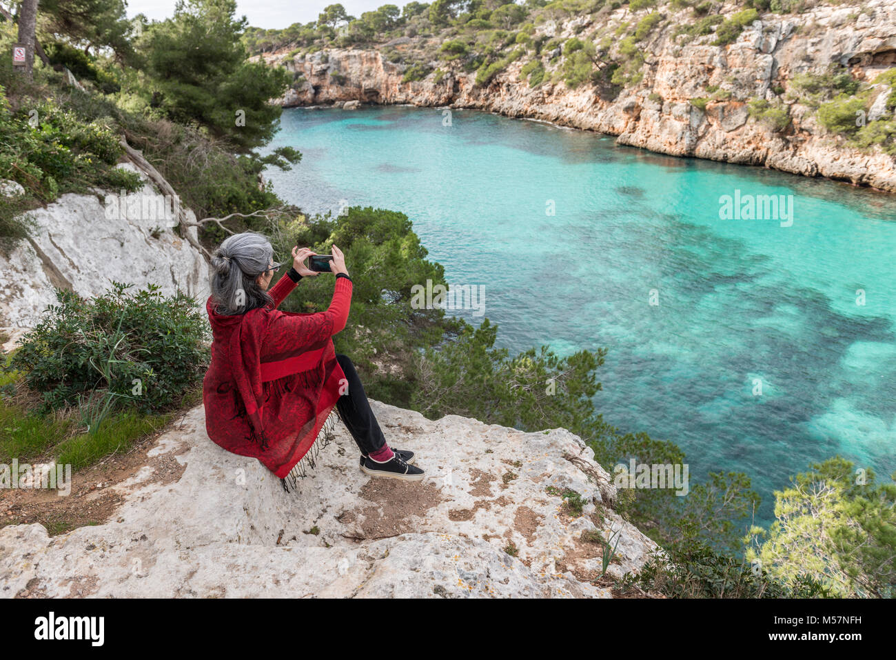 Eine junge brünette Frau mit ergrauendem Haar, einen roten Pullover Schal und ein Foto von der Blick auf Cala Pi auf der Insel Mallorca, Spanien. Stockfoto