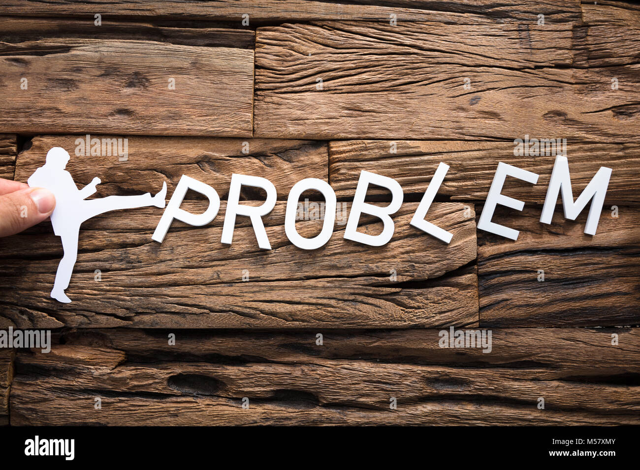 Nahaufnahme einer Hand, die Papier Geschäftsmann kicking Wort Problem auf Holz Stockfoto