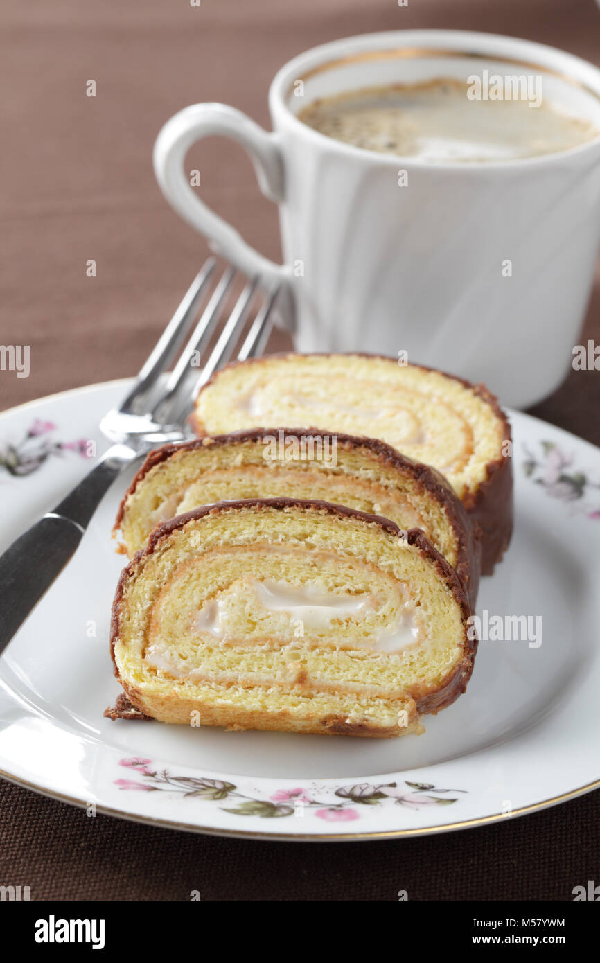 Schweizer Rolle mit Cremefüllung und Schokolade Topping gegen eine Tasse schwarzen Kaffee Stockfoto