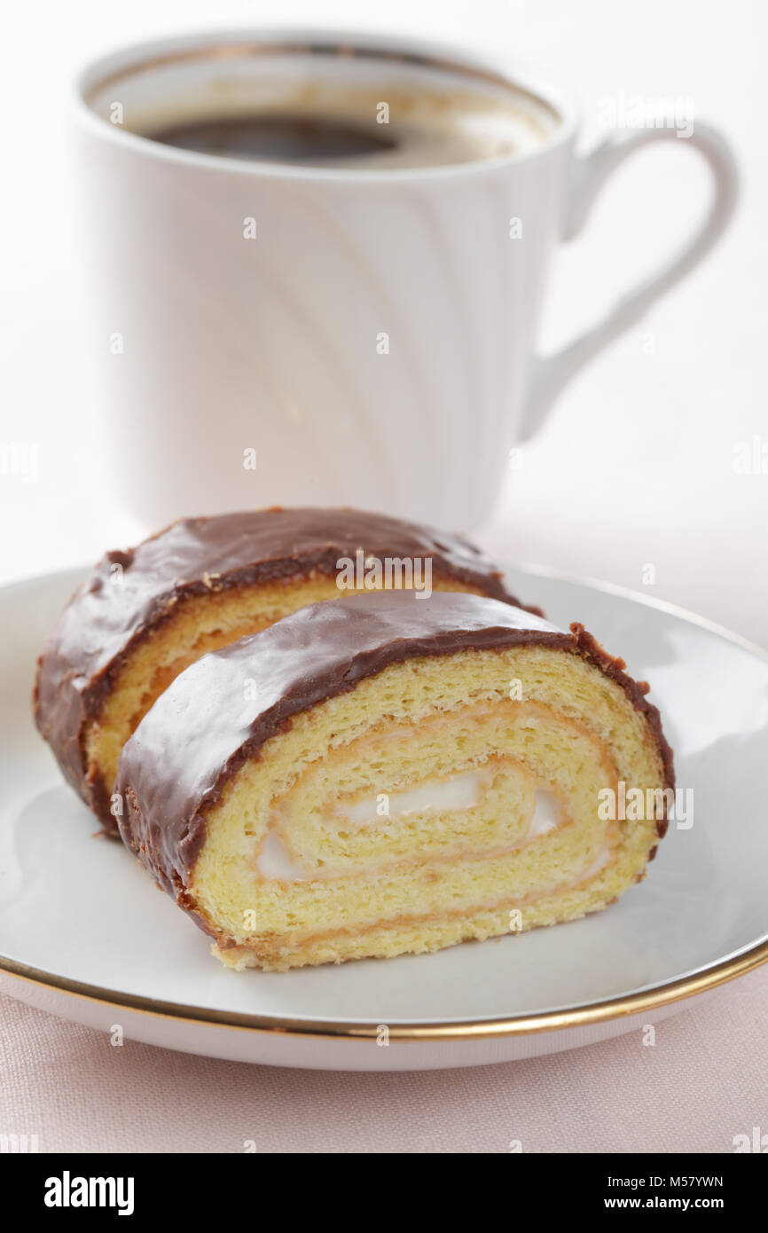 Schweizer Rolle mit Cremefüllung und Schokolade Topping gegen eine Tasse schwarzen Kaffee Stockfoto