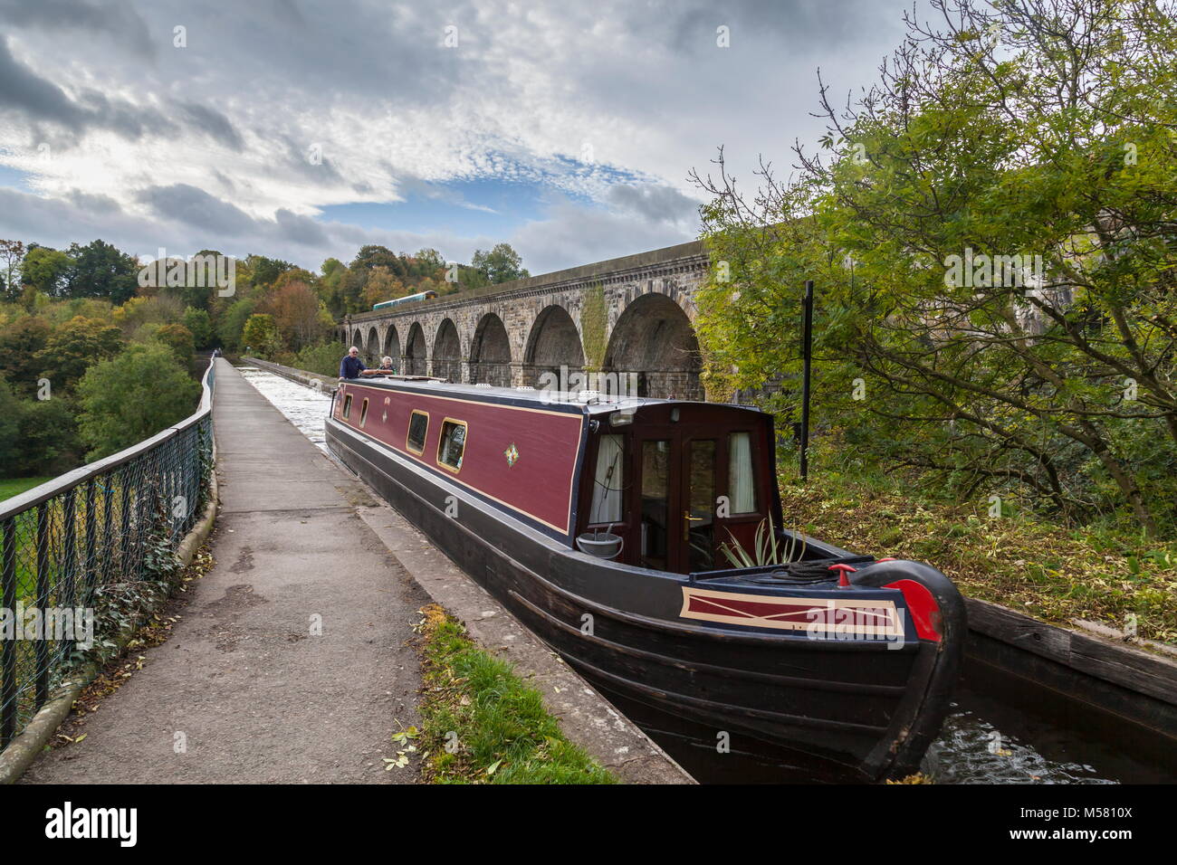 Ein schmales Boot Kreuze aus England nach Wales über die chirk Aqueduct während der frühen Herbst während ein Zug überquert die Henry Robertson erbaute Viadukt Stockfoto