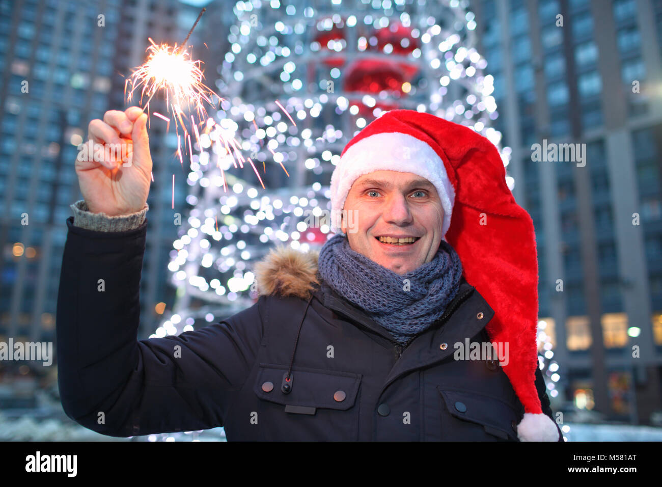 Reifer Mann in Santa's Hut holding Wunderkerzen gegen geschmückten Weihnachtsbaum im Freien Stockfoto