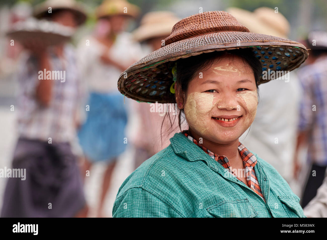 Eine Frau lächelt, als sie hilft, eine Straße in Kalay, einer Stadt in Myanmar. Die Frau trägt thanaka, ein kosmetischer einfügen, auf ihrem Gesicht. Stockfoto