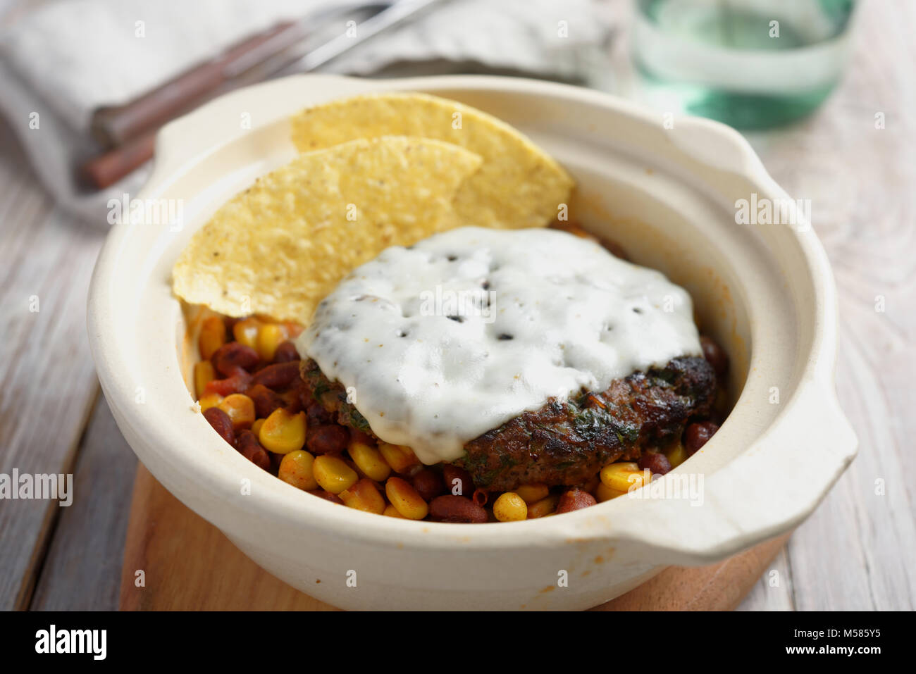 Beef Burger mit Käse, Mais und Bohnen garnieren schmelzen, und Mais Chips in einem rustikalen Pot Stockfoto