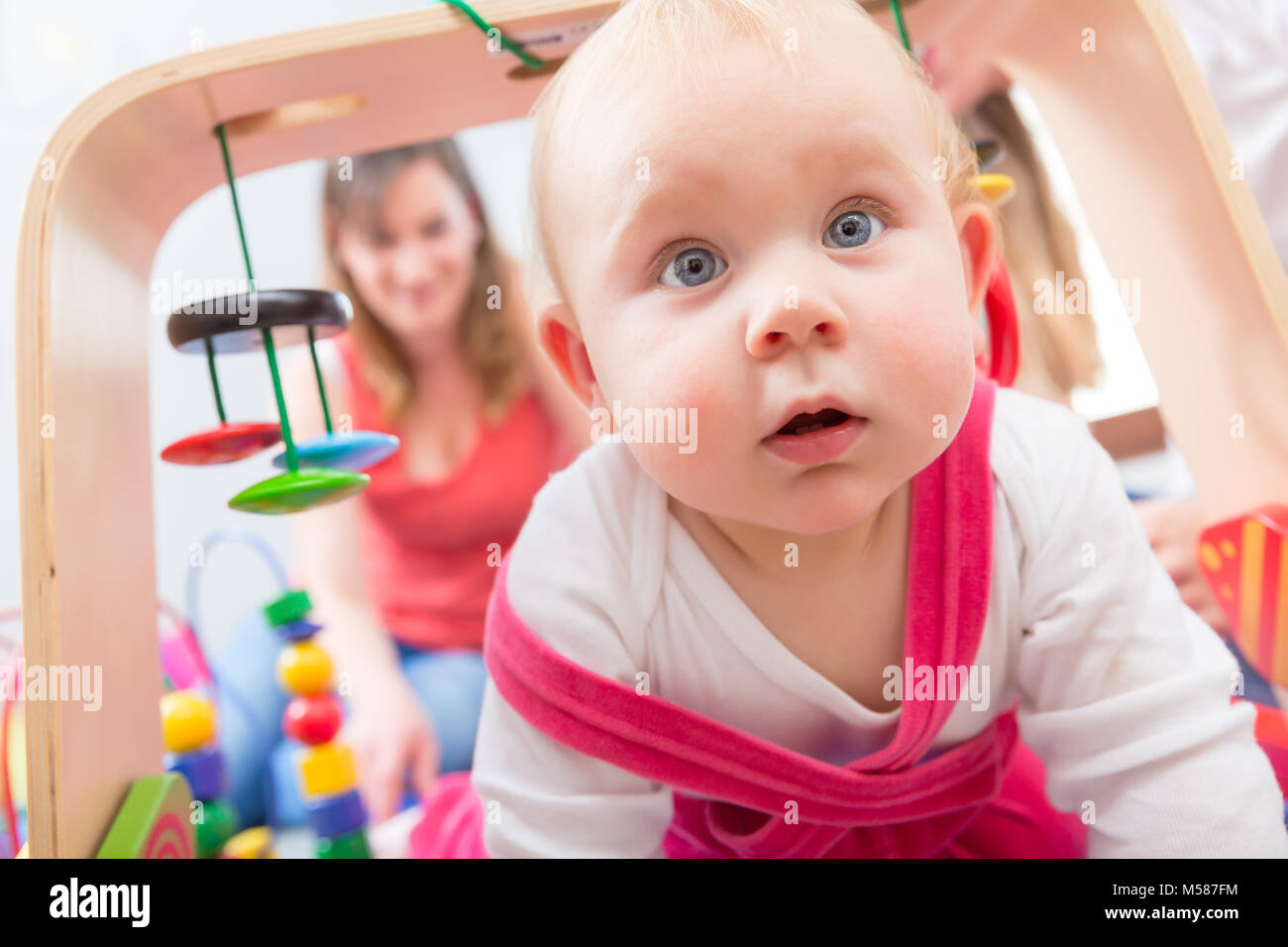 Nahaufnahme Porträt einer niedlichen Baby Mädchen mit blauen Augen und einem intelligenten Gesichtsausdruck, während sie auf dem Boden mit ihrer Mutter zu Hause Stockfoto