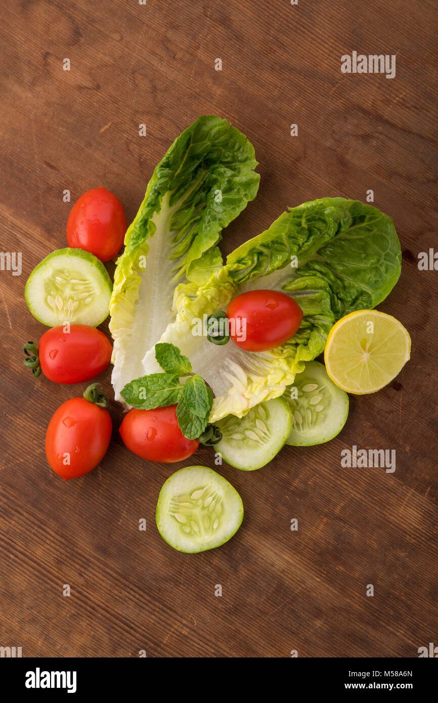 Gemüse: Frisches Grün Römersalat mit Baby Tomaten, Minze und Gurkenscheiben auf braunem Holz- Hintergrund Stockfoto