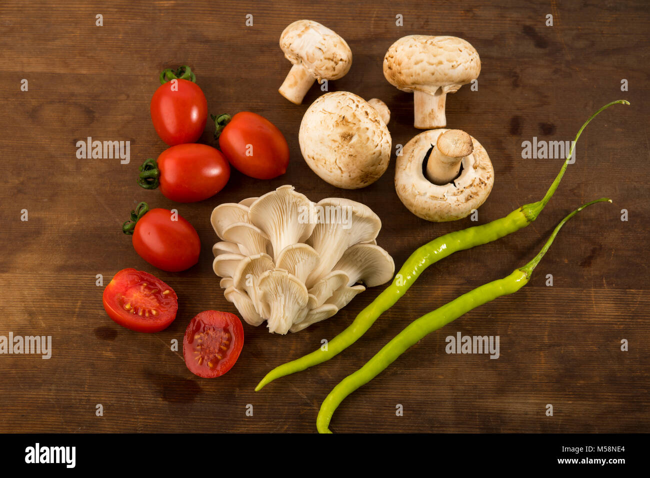 Gemüse: Blick von oben auf die Auster und Champignons mit roten Baby Tomaten isoliert auf braunem Holz- Hintergrund Stockfoto