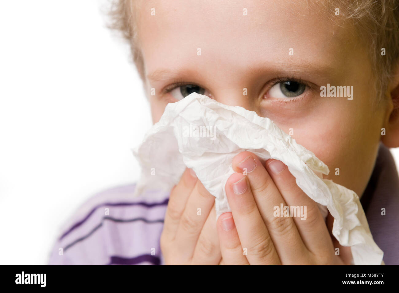 Frontale Großaufnahme eines siebenjährigen Kaukasischen Jungen, der mit einem Seidenpapier Nase puzend isoliert auf Weiss. Stockfoto