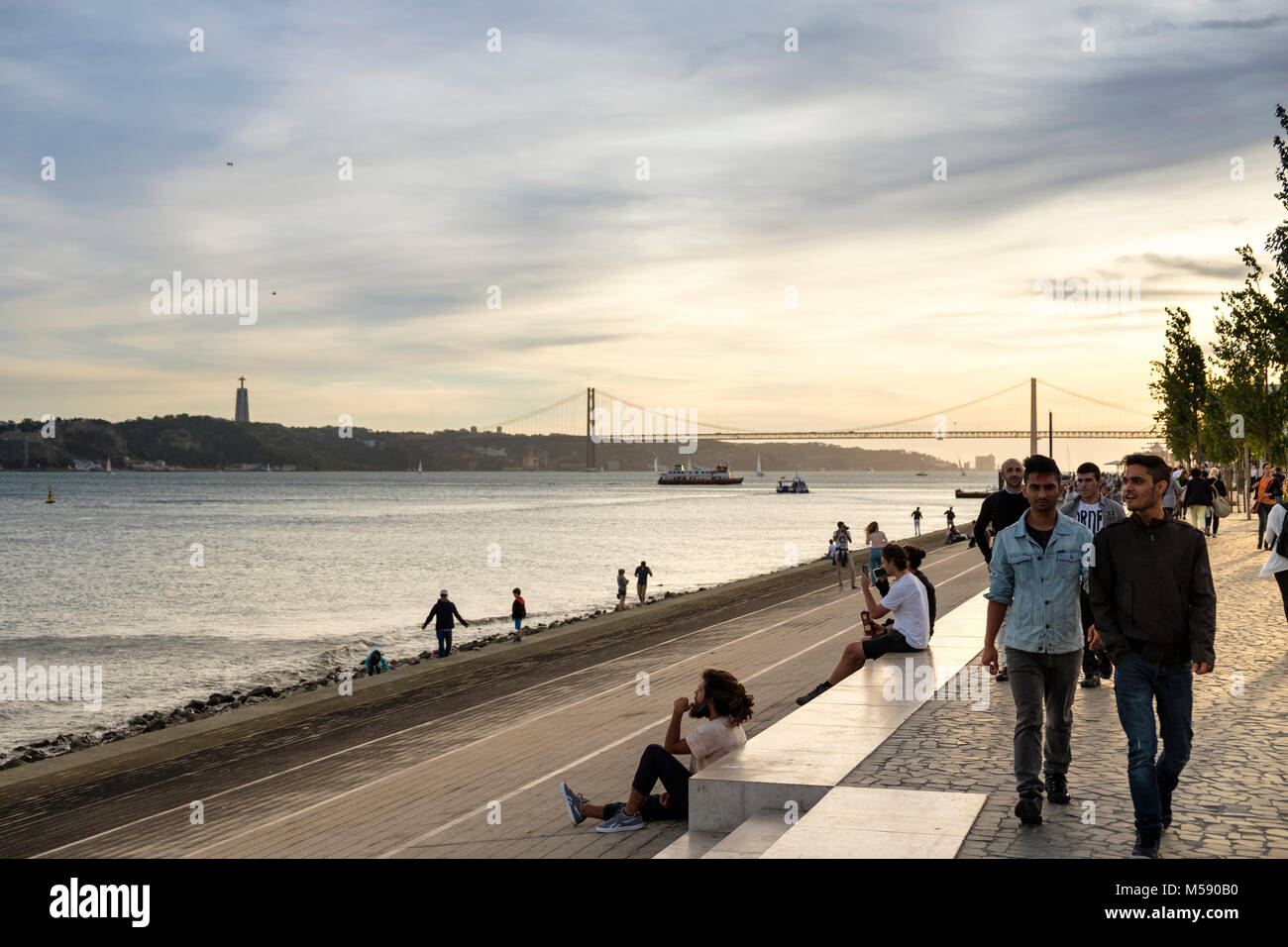 Das Leben auf der Straße auf den Fluss Tagus Prominade Lissabon mit Blick auf die Brücke Ponte 25 de Abril, Lissabon, Portugal Stockfoto