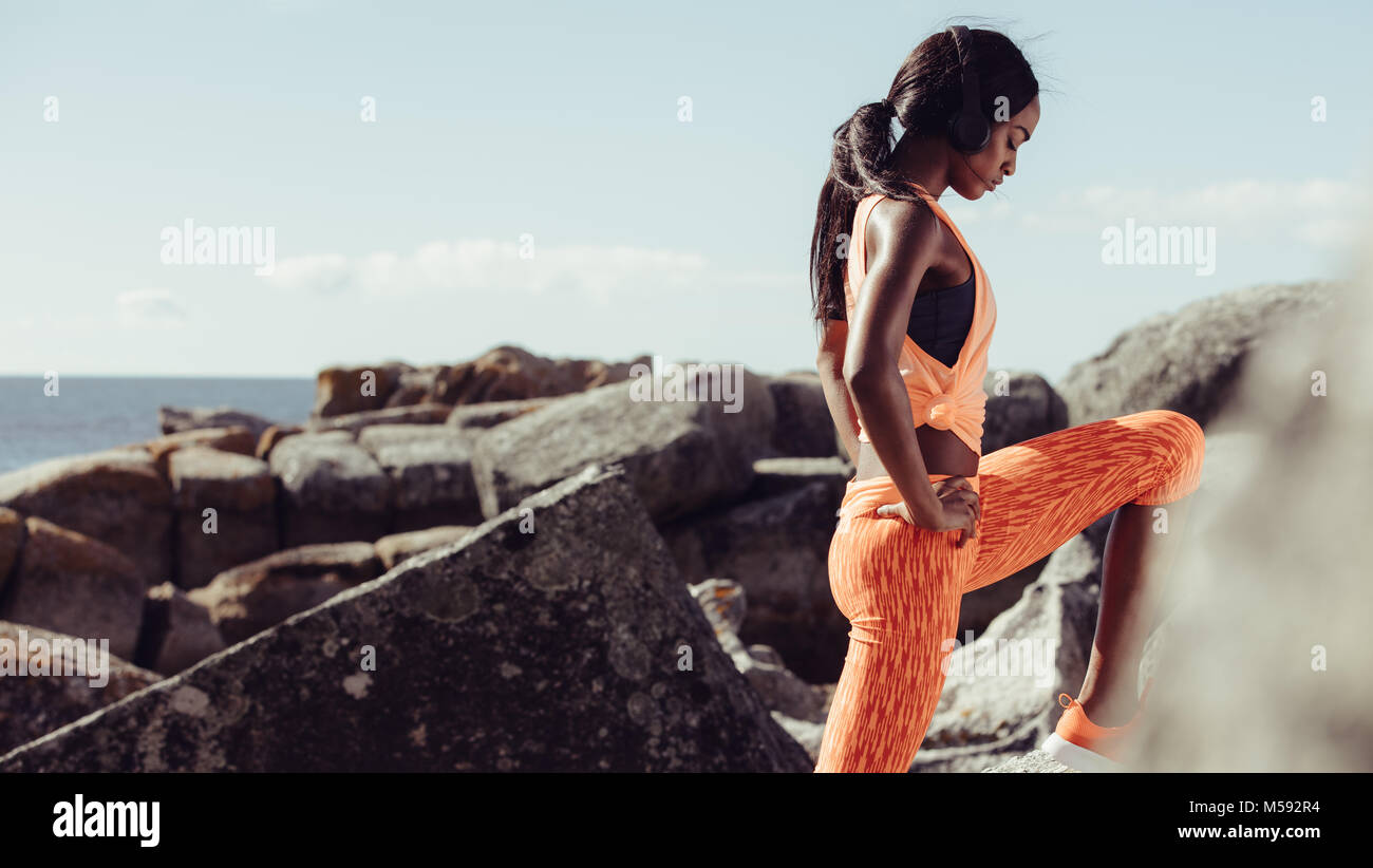 Gute junge afrikanerin beim Stretching-Workout. Fitnessmodell, das am Morgen am felsigen Strand trainieren kann. Stockfoto