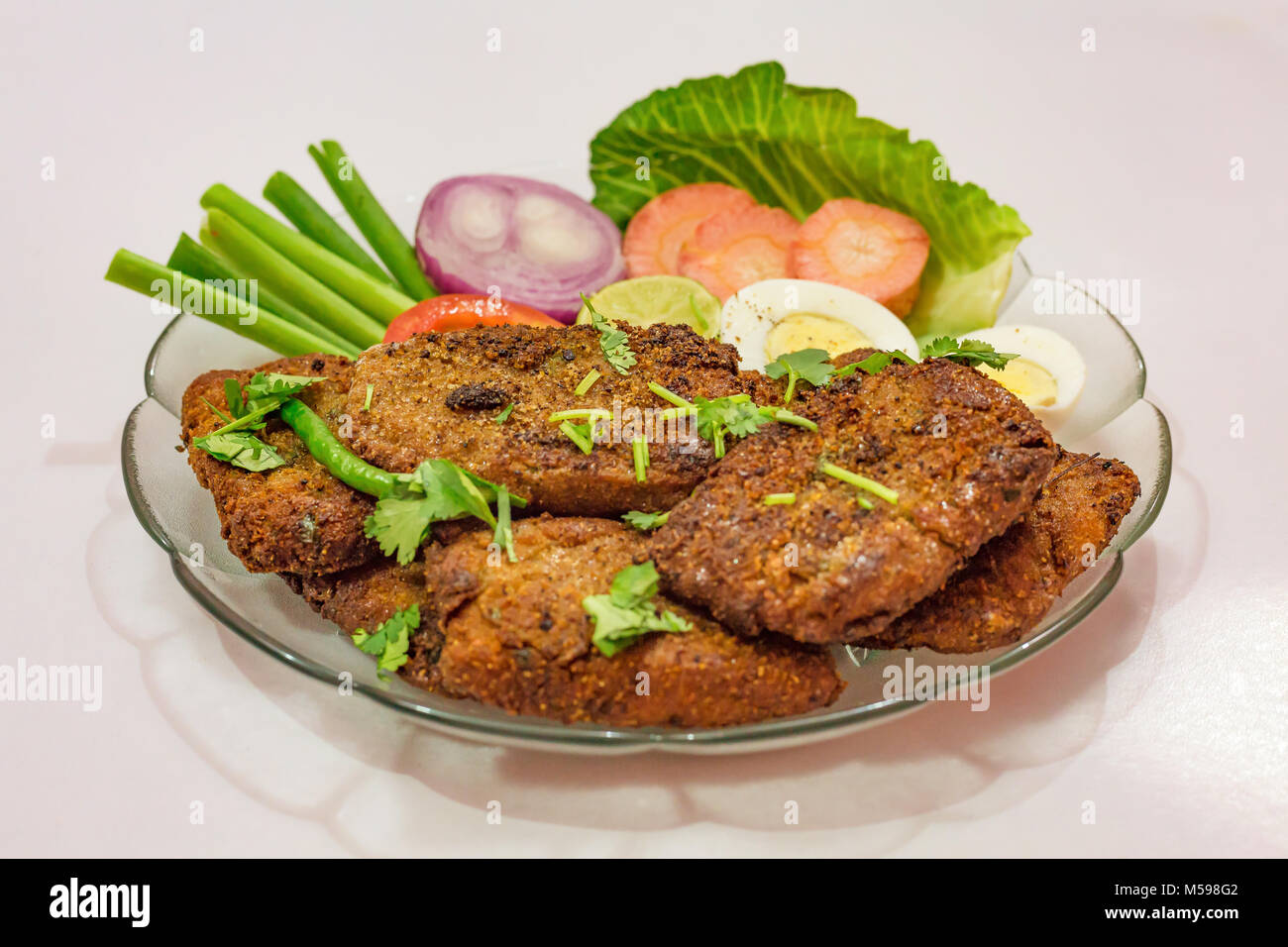 Leckere indische Bengali starter Gericht knusprige bhetki Fisch braten, garniert mit Bohnen mit Scheiben von Ei, Tomate, Karotte und Zwiebel. Stockfoto