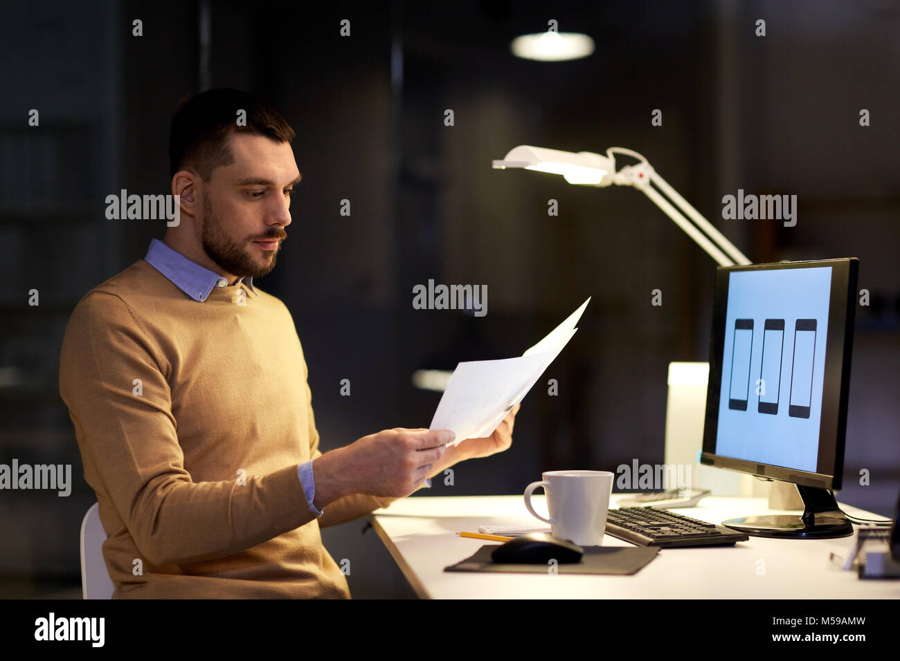 Mann mit Papieren und Computer funktioniert bei Nacht Büro Stockfoto