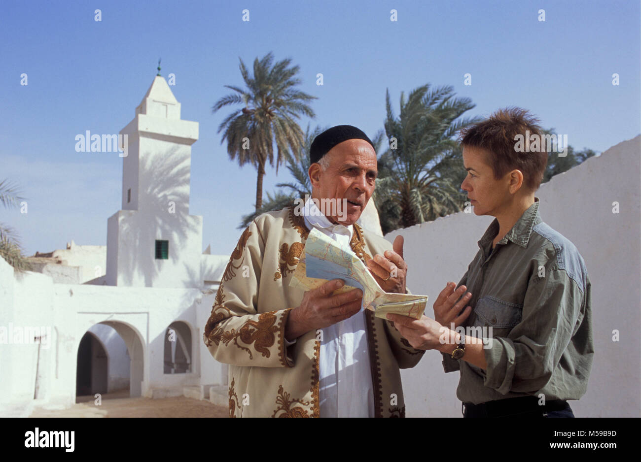 Libyen. Ghadames Oase. Sahara. Alte Stadt. Lokale Berber mann Richtung zu geben, Frau mit Karte. Minarett der Moschee. Unesco-Weltkulturerbe. Stockfoto