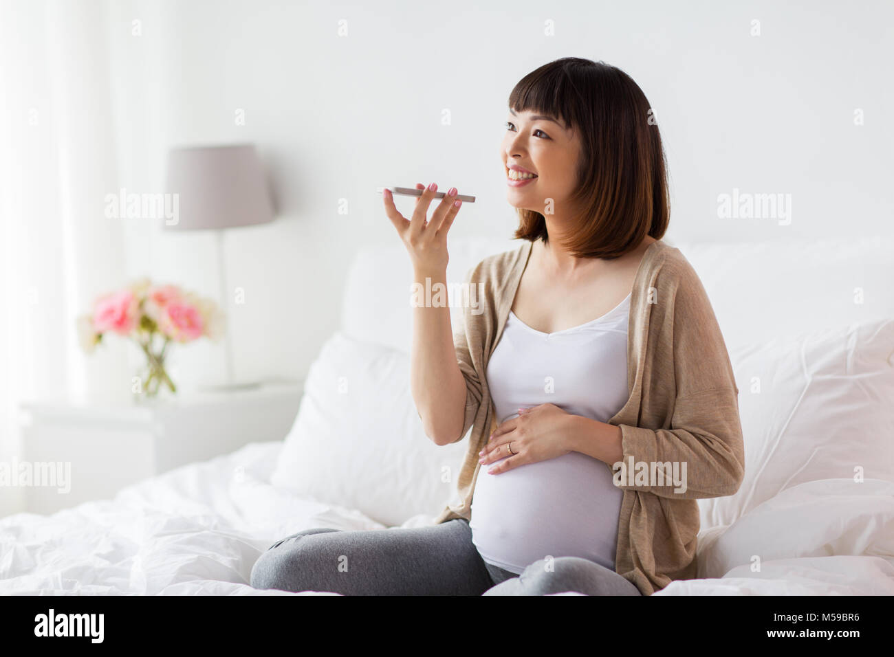 Schwangere Frau mit Voice-Recorder auf smartphone Stockfoto