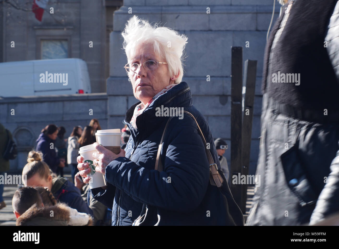 Eine ältere Frau mit zwei einwegbecher mit heißen Getränken mit Menschen im Hintergrund, Trafalger Square, London Stockfoto